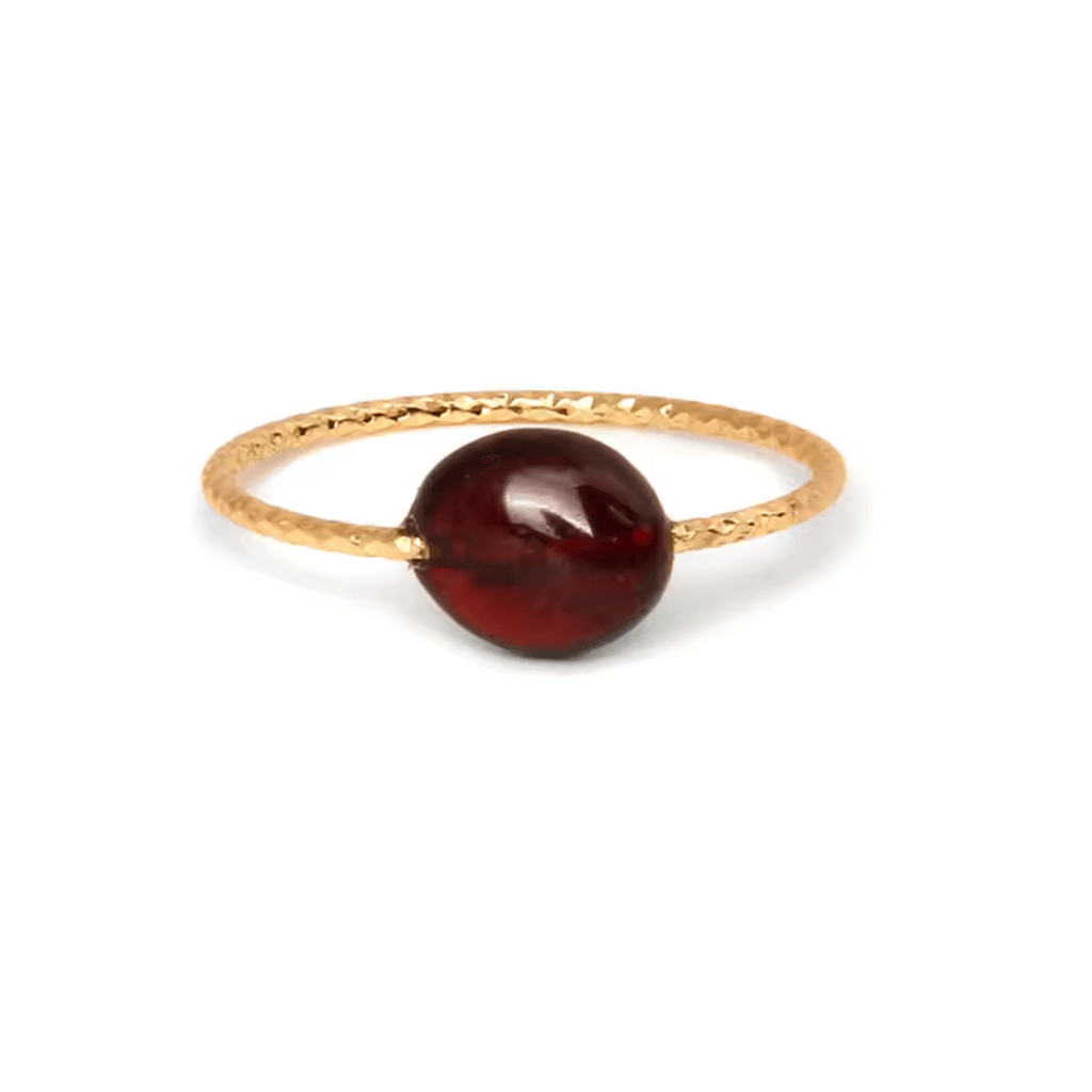 Elegant gold ring with a deep red gemstone on a thin, textured band